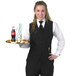 A woman wearing a black Henry Segal server vest holding a tray.