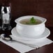 A white bowl of Silver Skillet cream of celery soup with a green leaf in it on a table with a spoon and a saucer.