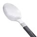 A WNA Comet Reflections Duet stainless steel look teaspoon with a black handle.