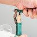 A person using a Franmara Duo-Lever corkscrew with a green enamel handle to open a bottle of wine.