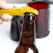 A person using a yellow Franmara Traveler's Corkscrew to open a brown beer bottle.