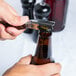A hand using a Laguiole Waiter's Corkscrew with a rosewood handle to open a bottle of beer.