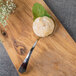 A Bon Chef stainless steel tasting spoon with food on a wooden surface.