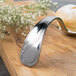 A Bon Chef silver bouillon tasting spoon with a flower design on a wooden surface.