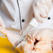 A person in white gloves using a Dexter-Russell narrow stiff boning knife to cut up a chicken.