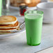 A stack of pancakes on a plate with a green Thunder Group Belize tumbler filled with milk.