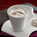 A Villeroy & Boch white porcelain mug filled with coffee topped with foam and a brown cinnamon stick on a saucer.