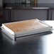 A white rectangular tray with a brown substance on it sitting on a metal tray with a rectangular white dish on it.