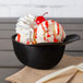 A close-up of a black mini baseball helmet bowl filled with ice cream, whipped cream, and a cherry.