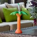 A clear plastic palm tree cup with orange liquid and a straw on a table.