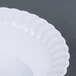 A close up of a Fineline Flairware white plastic bowl with a scalloped edge on a gray surface.