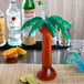 A drink in a 24 oz. clear palm tree shaped drink cup with a lime and colorful straw.