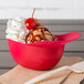 A red mini baseball helmet bowl filled with ice cream and a cherry.