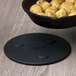 A black Lodge magnetic trivet holding a black pan with food on a wood surface.