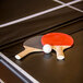 Two ping pong paddles and a ball on a Triumph pool table with a ping pong conversion top.