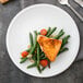 A Libbey Alpine White Porcelain coupe plate with a piece of salmon, green beans, and tomatoes on it.