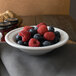 A Libbey alpine white porcelain fruit bowl filled with raspberries and blueberries on a table.