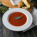 A Libbey alpine white porcelain soup bowl filled with tomato soup topped with a leaf.