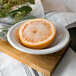 A Libbey Alpine White Porcelain grapefruit bowl with a half of a grapefruit on a table.