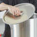 A hand holding a Vollrath stainless steel stock pot lid.
