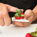 A person using a Victorinox paring knife to cut a strawberry on a white surface.
