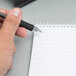 A hand using a black pen to write in a white wirebound reporter's notebook.