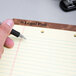 A person holding a pen writes on a TOPS wide ruled canary legal pad.