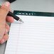 A hand using a pen to write on a TOPS Docket writing tablet.