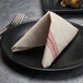A folded Hoffmaster FashnPoint white and red dishtowel print dinner napkin on a black plate.