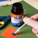 A hand using blue and yellow scissors to cut paper on a table next to a bottle of Elmer's No-Wrinkle Rubber Cement.