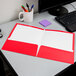 A red Oxford 2-pocket folder on a white surface next to a computer.