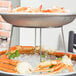A Choice chrome plated steel display stand holding a large plate of seafood on ice with crab legs.