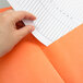 A person holding an orange Oxford embossed paper pocket folder.