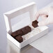 A hand holding a 6" x 3 1/4" white candy box with a chocolate window