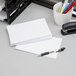 A stack of Oxford white ruled index cards on a table next to a white mug with pens in it.