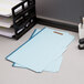 A stack of blue Pendaflex legal size fastener folders on a table.