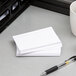 A stack of Oxford white ruled index cards on a white surface next to a pen and a cup.