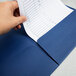 A hand placing a piece of paper in a navy blue Oxford pocket folder.