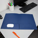 An Oxford navy blue paper pocket folder on a desk with pens in a cup.