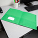 A light green Oxford 2-pocket folder on a desk with pens in a white mug.