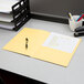 A yellow Oxford letter size pocket folder on a desk with paper and pens in a cup.