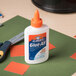 A white bottle of Elmer's Glue-All on a green surface with a yellow and orange cap.