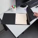 A hand opening a black Cardinal horizontal easel binder on a black surface.