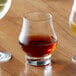 A Reserve by Libbey Distill whiskey glass filled with brown liquid on a table with a glass of wine.