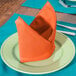 An orange Intedge cloth napkin folded on a plate.