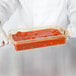 A person in white gloves holding a Cambro amber plastic food pan with red sauce on a counter.