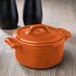 A small orange Bon Chef cocotte with a lid.