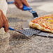 A person using a GI Metal perforated triangular pizza server with a blue handle to cut a pizza.