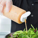 A person using a Tablecraft clear plastic squeeze bottle to pour salad dressing onto a salad.