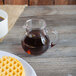 A glass Spiegelau Bodega pitcher filled with brown liquid on a table with a plate of waffles.